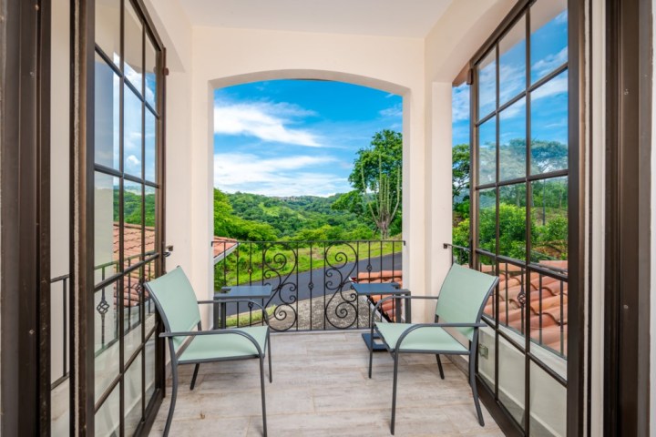 Two chairs on a balcony overlooking green hills and a bright blue sky.