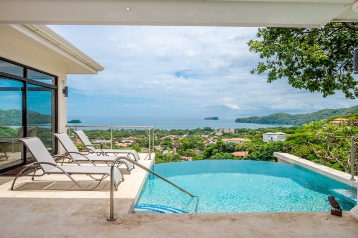 Infinity pool with lounge chairs overlooking ocean and lush landscape.