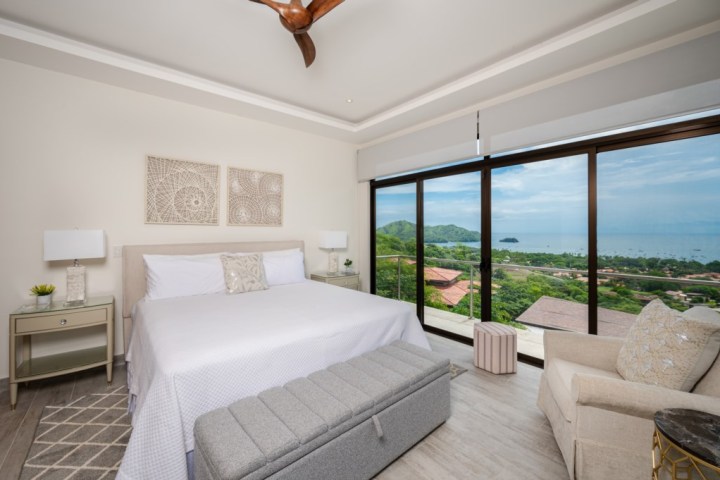 Bright bedroom with ocean view, large bed, two lamps, and a ceiling fan.