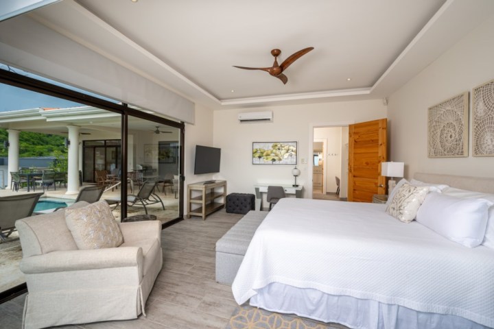 Modern bedroom with a large bed, TV, and outdoor pool view through glass doors.