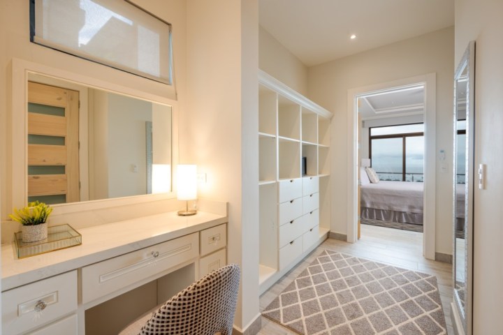 Elegant dressing area with vanity, mirror, shelves, and view into bedroom.