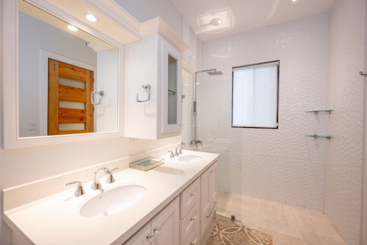 Modern bathroom with double sink vanity, large mirror, walk-in shower, and textured white tile walls.