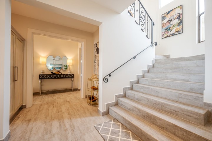 Elegant foyer with wooden stairs, ornate black rail, and a console table with two lamps and a mirror.