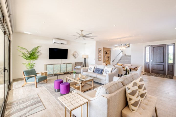 Spacious living room with modern furniture, TV, large windows, and staircase in a bright interior.
