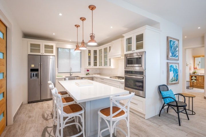 Modern kitchen with white cabinets, island, pendant lights, and stainless steel appliances.