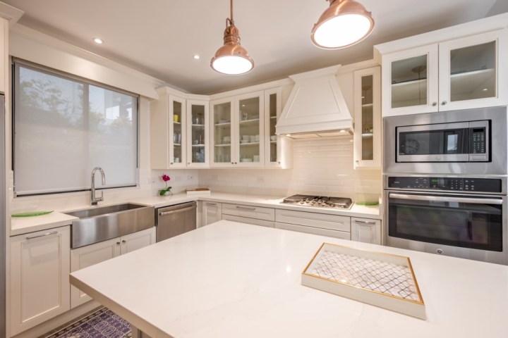 Modern kitchen with white cabinets, island, stainless steel appliances, and two pendant lights.