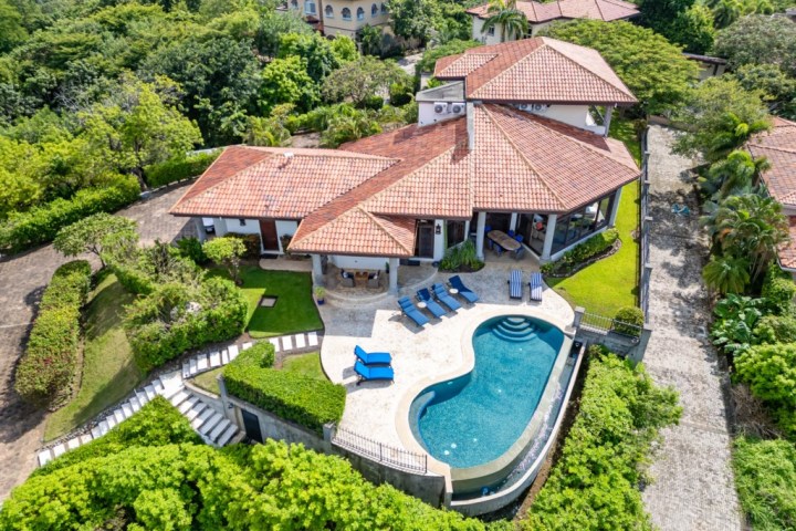 Aerial view of a villa with a red-tiled roof, pool, and lush green surroundings.