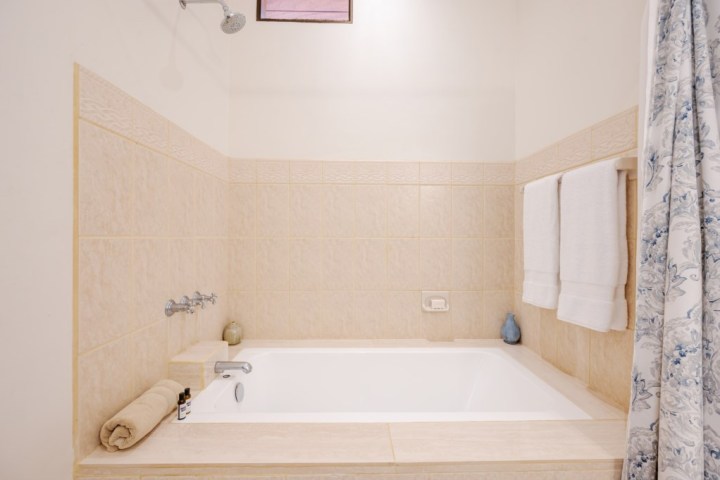 Bathroom with beige tile, a bathtub, and towels on a rack.