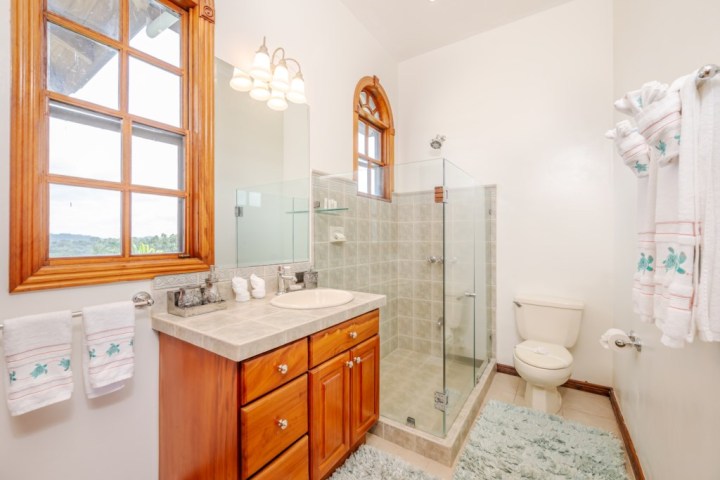 Bathroom with wooden cabinets, glass shower, and window with a view.
