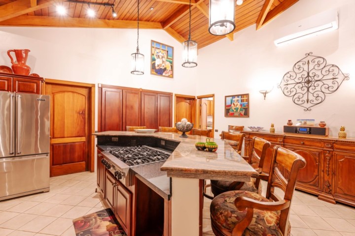 Spacious kitchen with wooden cabinets, stainless steel fridge, and granite countertop under vaulted ceiling.