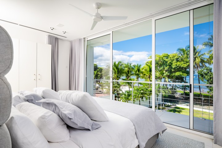 Bright bedroom with large windows, ocean view, and palm trees outside.