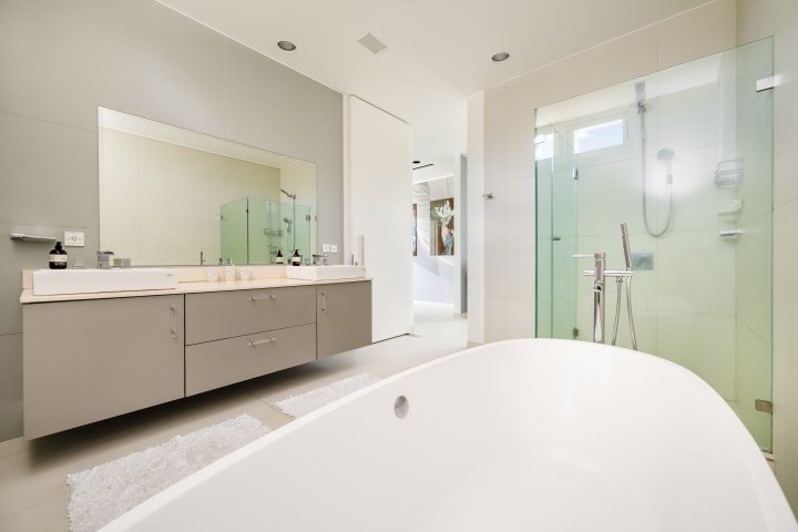 Modern bathroom with bathtub, glass shower, and large mirror above a double sink vanity.