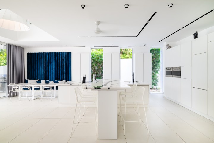 Modern white kitchen with blue velvet seating, island, and large windows.