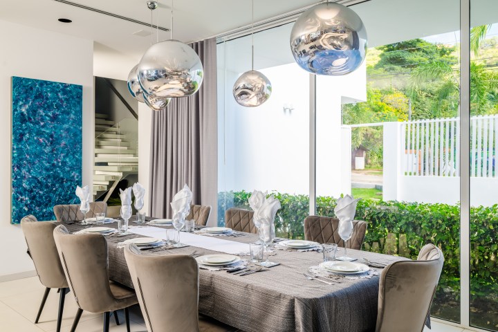 Elegant dining room with a table set for eight, silver globular lights, large window, and abstract painting.