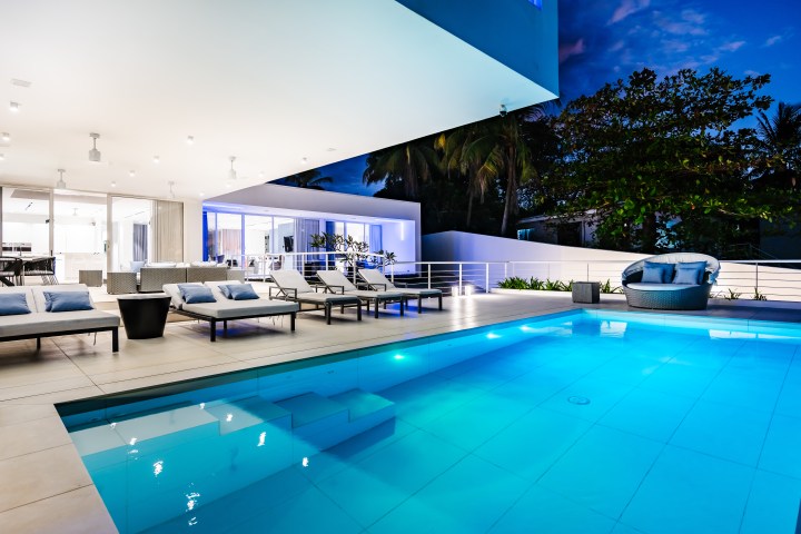 Modern patio with pool, lounge chairs, and outdoor lighting at night.