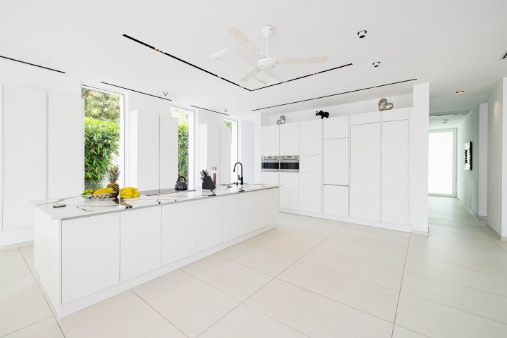 Modern white kitchen with island counter, built-in appliances, and large windows.