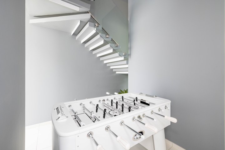 White foosball table near modern floating staircase against gray wall.