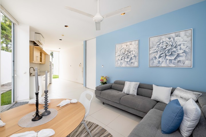Modern living room with gray sofa, blue accent wall, and kitchen area in background.