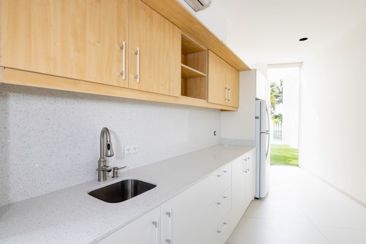 Modern kitchen with light wood cabinets, white countertops, and stainless steel faucet.