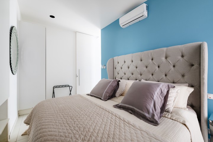 Bedroom with blue wall, tufted headboard, beige bedding, and a wall-mounted air conditioner.