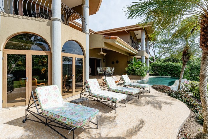 Patio with lounge chairs, arched windows, and a pool surrounded by palm trees.