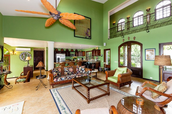 Spacious green living room with high ceilings, wicker furniture, and ceiling fan.