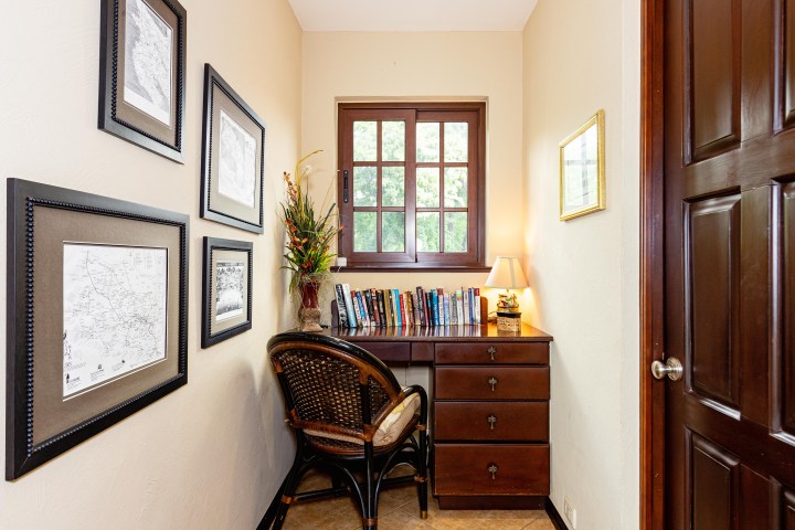 Cozy home office nook with desk, chair, books, lamp, and framed pictures.