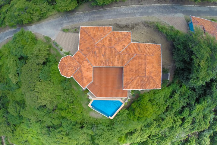 Aerial view of house with red roof and pool, surrounded by dense greenery.