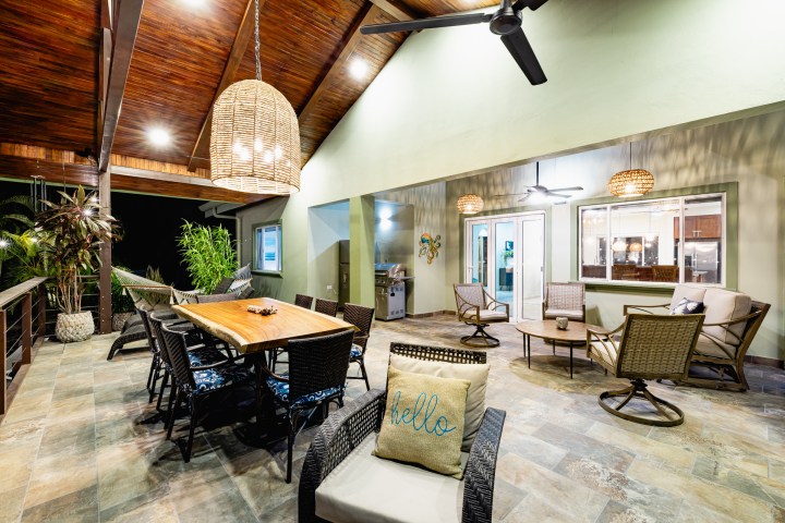 Outdoor patio with table, chairs, ceiling fans, and decorative lights under a wooden ceiling.