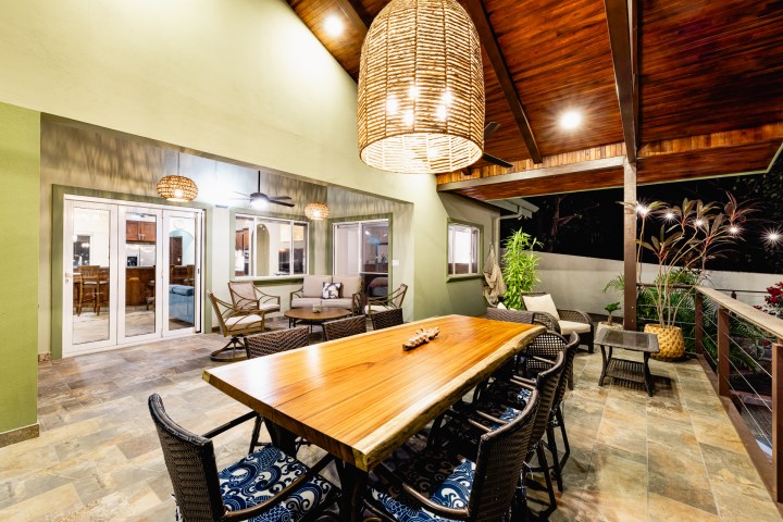 Modern patio with wooden dining table, wicker chairs, wicker lights, and outdoor seating area.