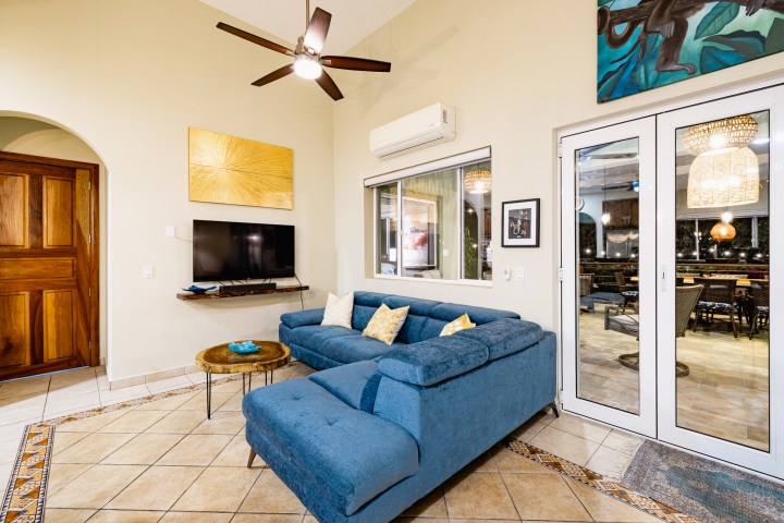 Living room with blue sofa, wall-mounted TV, and glass doors to a dining area.