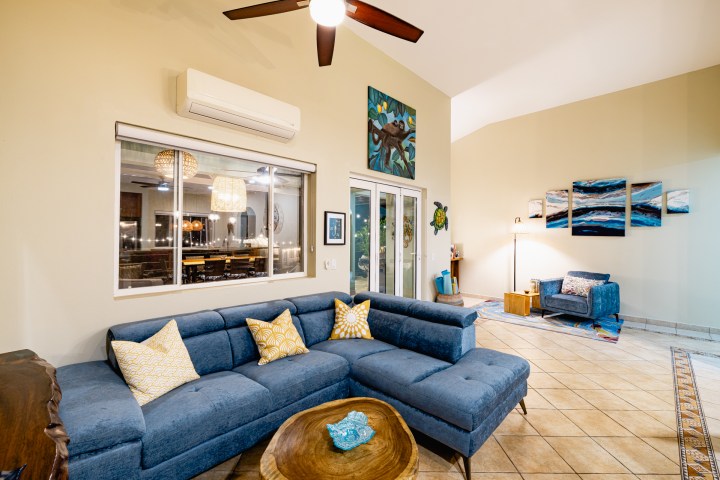 Living room with blue sectional, art on walls, ceiling fan, and large window.