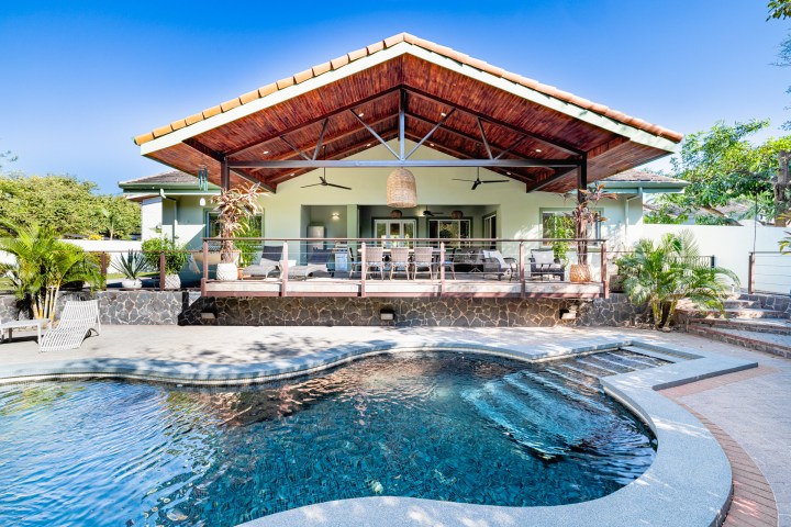 Poolside view of a modern house with a large patio and wooden roof.