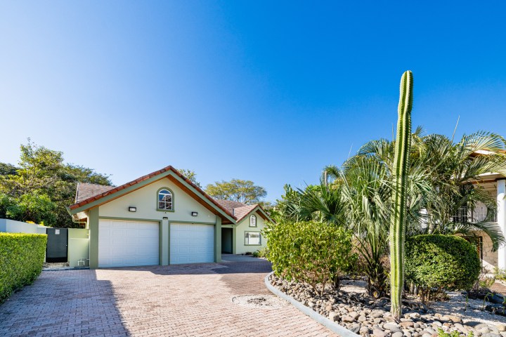 House with a red roof, double garage, and garden with cactus under a clear blue sky.
