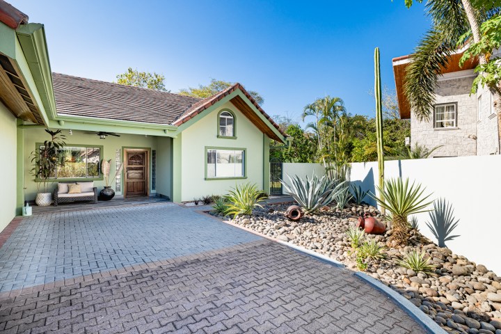 Green house with tile roof, driveway, and desert landscaping with succulents and cacti in foreground.