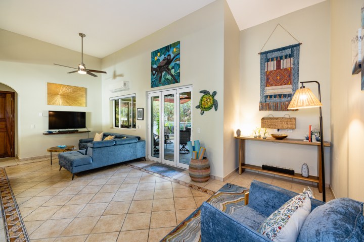 Spacious living room with blue sofas, artwork, TV, ceiling fan, and sliding doors leading to an outdoor area.