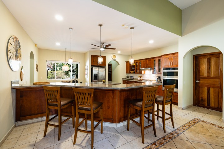 Spacious kitchen with wood cabinets, island, bar stools, pendant lights, and ceiling fan.