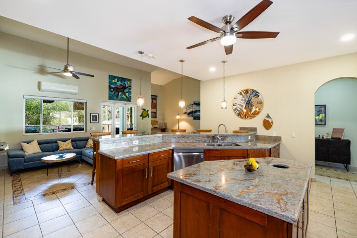 Modern kitchen with marble island, ceiling fans, pendant lights, and adjacent living area with sofa.
