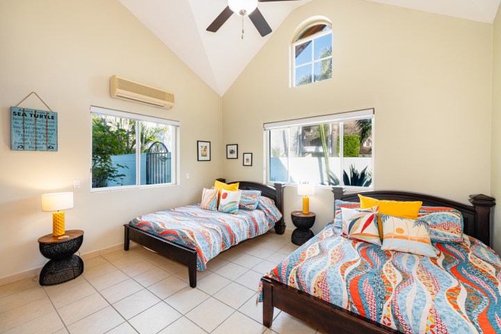 Bright bedroom with two beds, colorful bedding, and large windows.