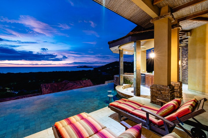 Luxury patio with striped loungers overlooking ocean at sunset.