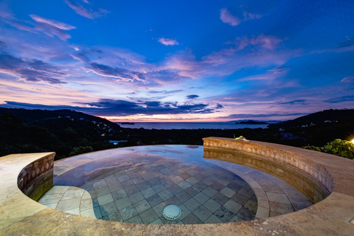 Circular infinity pool with ocean view at sunset.