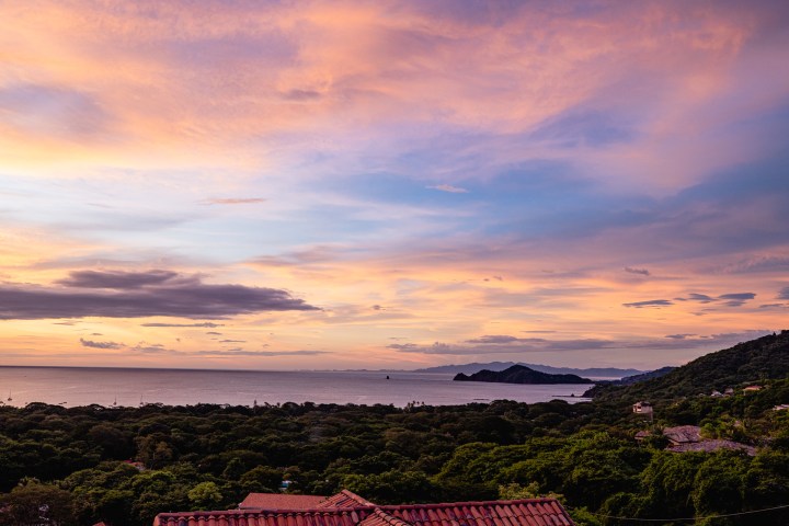 Colorful sunset over ocean and landscape with hills.