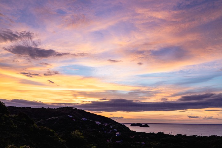 Vibrant sunset over a coastal landscape with silhouetted hills and colorful clouds.