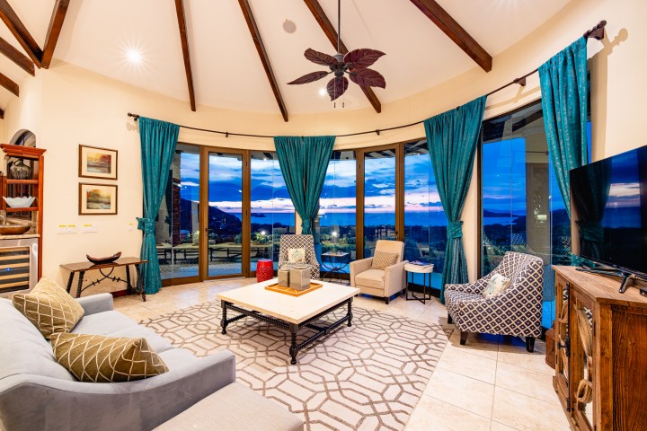 Cozy living room with large windows, blue curtains, and modern furniture at sunset.