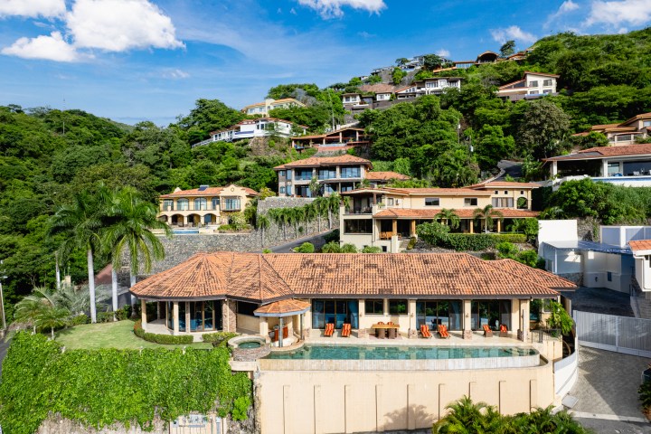 Luxury hillside villas surrounded by lush greenery and clear blue sky.