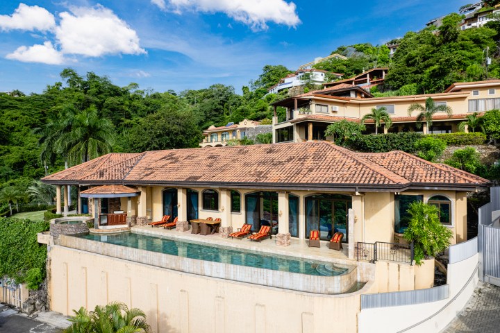 Luxury villa with pool on hillside, surrounded by tropical greenery.