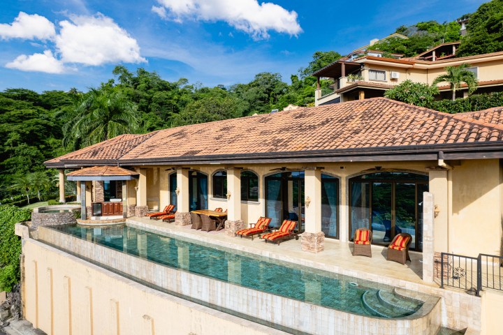Luxury villa with infinity pool and patio, surrounded by lush greenery.