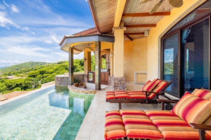 Luxury patio with striped loungers, infinity pool, and scenic view.