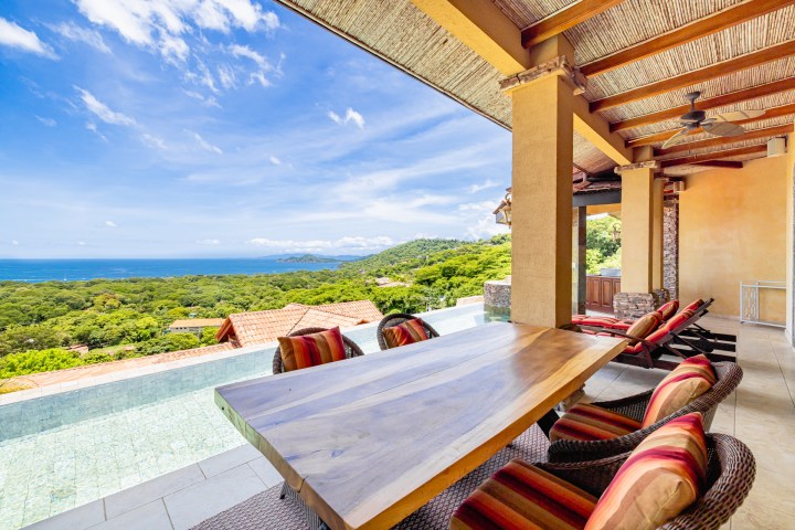 Outdoor patio with table, chairs, infinity pool, and ocean view.