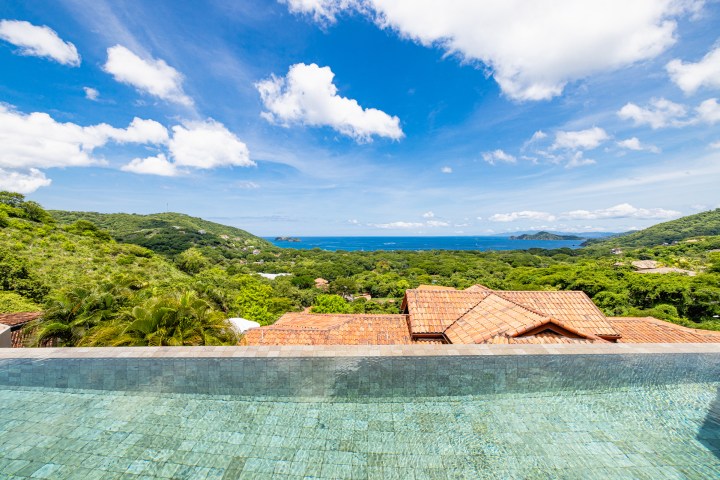 Infinity pool overlooking ocean and lush hills under a blue sky.
